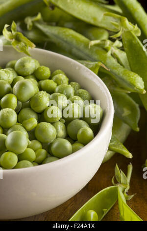 Fresco verde piselli con baccelli nella ciotola sul tavolo di legno Foto Stock