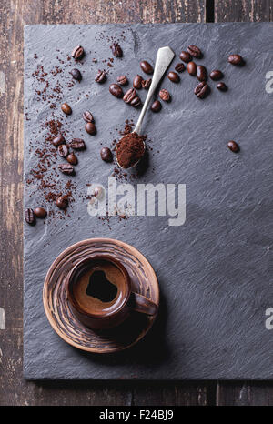 Ceramica marrone tazza di caffè e tè freschi cucchiaio con il caffè macinato e i chicchi di caffè su nero ardesia come sfondo. Con spazio di copia Foto Stock