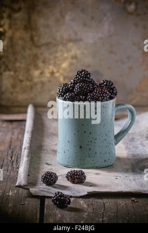 Avvistato in ceramica blu tazza di mirtilli (dewberry), al vecchio tavolo di legno con stagno. Stile rustico. Foto Stock