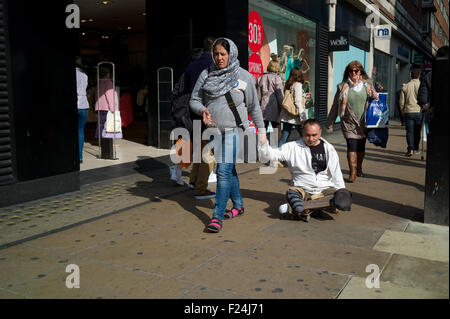 Un mendicante legless essendo tirato giù Oxford Street da una donna su uno skateboard. Foto Stock