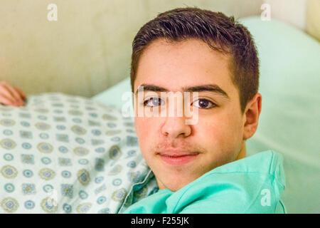 Caucasian Teen boy con bretelle abbracciando cuscino nel letto Foto Stock