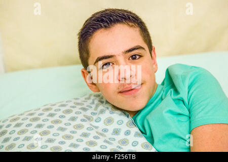 Caucasian Teen boy con bretelle abbracciando cuscino nel letto Foto Stock