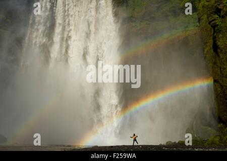 L'Islanda, South Coast, Skogafoss, bambini jumping sotto Skogafoss cascata, doppio arcobaleno Foto Stock