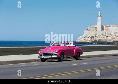 Cuba, Ciudad de la Habana Province, La Havana, vettura americana sul Malecon e il faro del Castillo de los Tres Reyes Magos in background Foto Stock