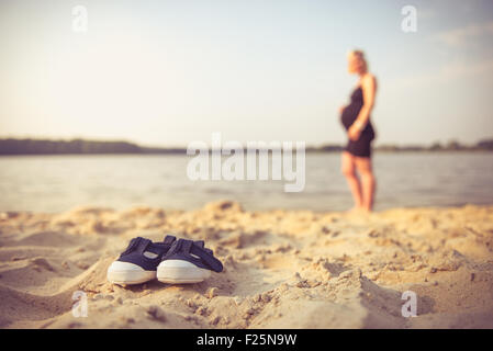 Foto del minuscolo scarpe per bambini e di una futura mamma in background. Foto Stock