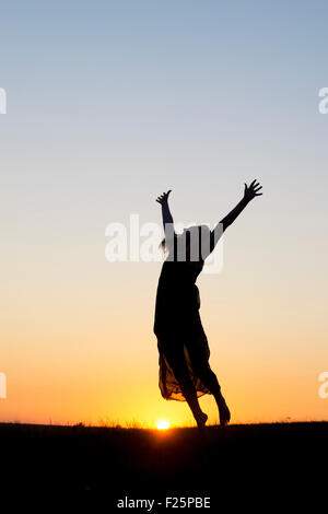 Ragazza adolescente energeticamente divertirsi saltando intorno al tramonto. Silhouette Foto Stock