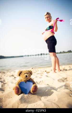 Foto di un orso di peluche in primo piano e bella donna incinta in background. Foto Stock