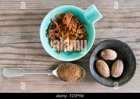 Un piatto di tre Nutmeg, un piatto di lame di Mace e un cucchiaio di Nutmeg macinato su un tavolo da cucina in legno Foto Stock