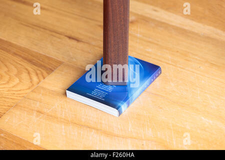 Gamba di un tavolo traballante supportato da un libro Foto Stock