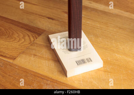 Gamba di un tavolo traballante supportato da un libro Foto Stock