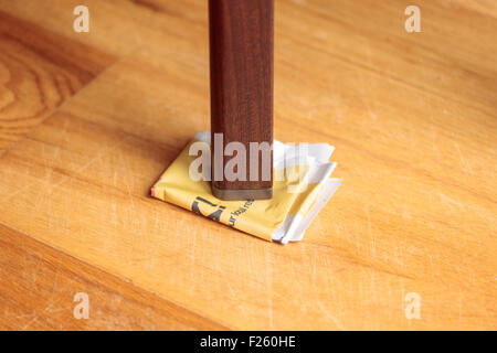 Gamba di un tavolo traballante supportato da carta piegata Foto Stock