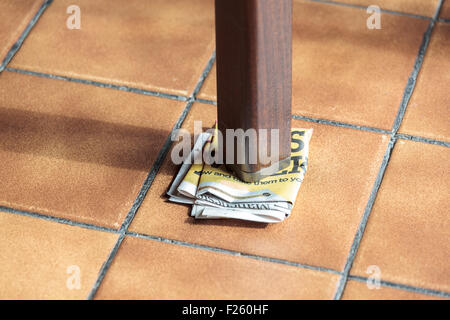 Gamba di un tavolo traballante supportato da carta piegata Foto Stock