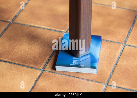 Gamba di un tavolo traballante supportato da un libro Foto Stock