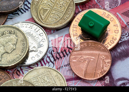 Modello di imitazione Verde casa di plastica con un tetto poggia sulla sommità della British monete di valori diversi e di colori e una cinquantina di pound n Foto Stock