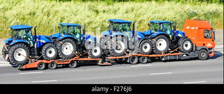 Distribuzione del trattore quattro blu nuovi Trattori marchio New Holland in fabbrica sul fresco hgv caricatore basso autocarro autocarro e rimorchio articolato Essex England Regno Unito Foto Stock