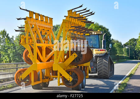 Un agricoltore che guida un trattore Caterpillar Challenger di grandi dimensioni che traina un'attrezzatura agricola con erpice a dischi ripiegati in una stretta corsia di campagna Essex Inghilterra Regno Unito Foto Stock