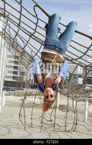 Giovane donna pendente da una rete da arrampicata nel parco giochi, Monaco di Baviera, Germania Foto Stock