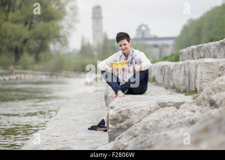 Donna matura seduti sui gradini e la lettura di libro, Baviera, Germania Foto Stock