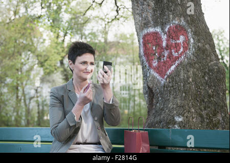 Donna matura su una panchina nel parco il rossetto per la sua data, Baviera, Germania Foto Stock