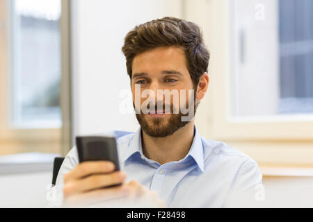 Allegro uomo barbuto con il suo smartphone in un ufficio moderno Foto Stock