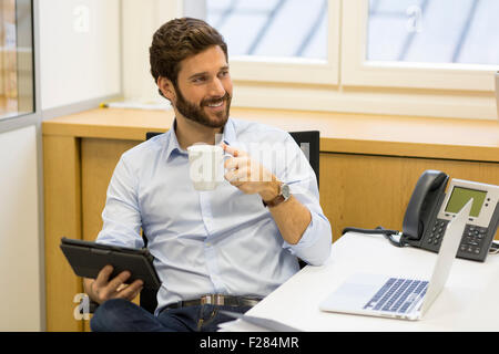 Ritratto di imprenditore sorridente holding tazza da caffè in ufficio Foto Stock