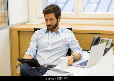 Ritratto di imprenditore tenendo tazza di caffè e usando tavoletta digitale in ufficio Foto Stock