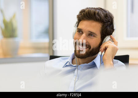 Imprenditore sorridente ascolto di musica con cuffie Foto Stock