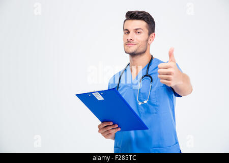 Ritratto di un bel maschio medico tenendo negli appunti e mostrando il pollice in alto isolato su sfondo bianco Foto Stock