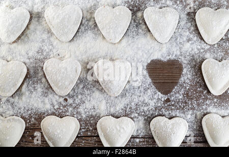 A forma di cuore ravioli cosparsa di farina su un tavolo di legno. Gnocchi di cottura. Vista superiore Foto Stock