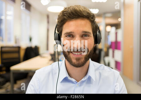 Ritratto di sorridere uomo d affari che indossa la cuffia in office Foto Stock