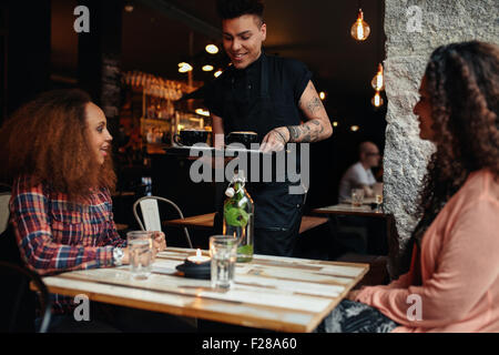 Traino di giovani donne seduti ad un ristorante con cameriere che serve caffè. Amici di sesso femminile presso la caffetteria. Foto Stock