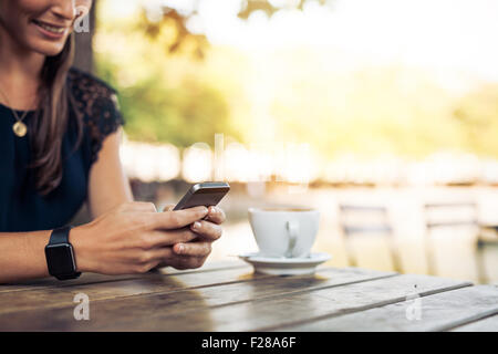 Donna che indossa un smartwatch tramite telefono cellulare al cafe'. Mano femminile con lo smartphone e caffè. Foto Stock