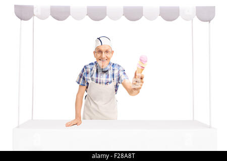 Senior ice cream vendor in piedi dietro a una fase di stallo e dando un gelato verso la telecamera isolata su sfondo bianco Foto Stock