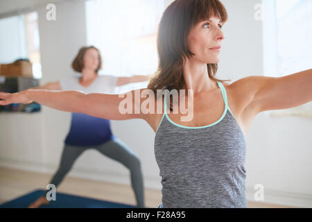Fitness trainer facendo il guerriero pongono durante la lezione di yoga. Insegnante di Yoga di eseguire Virabhadrasana posizione in palestra con persone n b Foto Stock