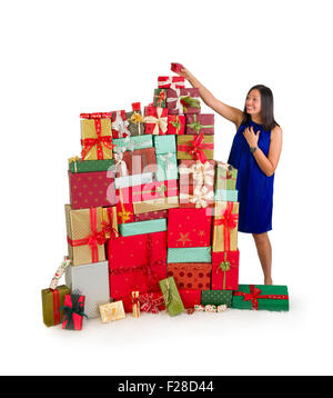 Giovane donna mettendo un piccolo dono sulla sommità di un enorme pila di regali di natale Foto Stock