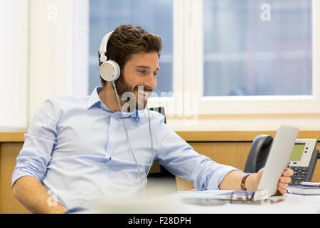 Barbuto imprenditore con cuffie e portatile in ufficio Foto Stock