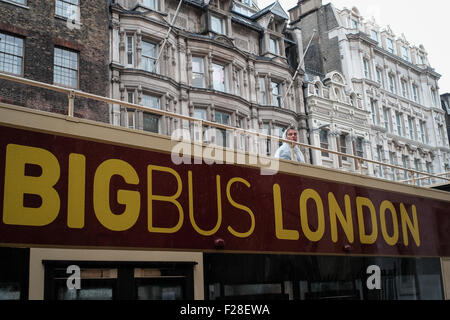 Un uomo si erge una solitaria figura sulla parte superiore di una apertura di autobus di Londra sotto la pioggia che indossa una pioggia di mac Foto Stock