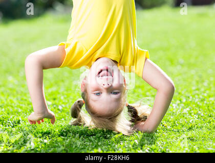 La ragazza del bambino in piedi capovolto sul suo capo su erba in estate Foto Stock