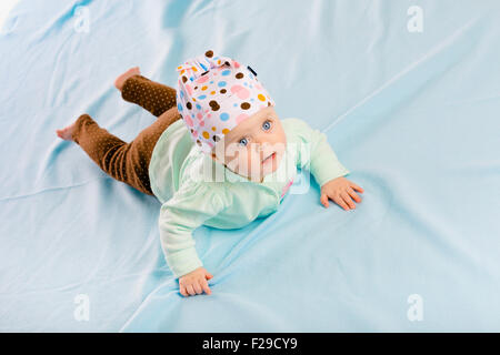 Il blue-eyed baby in hat strisciando sul blue plaid Foto Stock