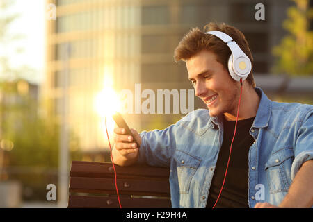 Uomo felice ascolto della musica da un telefono intelligente con un calore del tramonto sullo sfondo della città Foto Stock