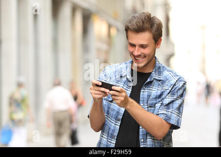 Uomo felice giocando con uno smart phone in strada Foto Stock