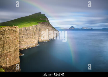 Gigantesche scogliere sul mare poco dopo la tempesta su Isole Faerøer con un arcobaleno. Lunga esposizione. Foto Stock