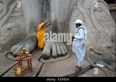 Un pellegrino jaïn ( l'uomo vestito di arancione) è adorare Gomateshwara, uno dei principali jaïn leader spirituale ( India) Foto Stock