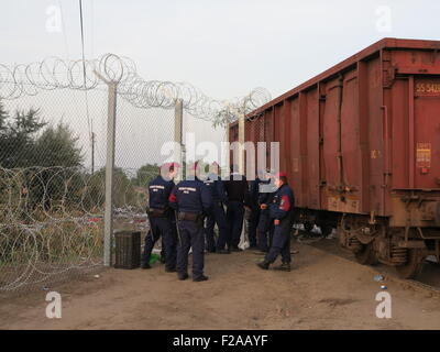 Roeszke, Ungheria. Xv Sep, 2015. Ungherese degli ufficiali di polizia a guardia della ultima sezione della recinzione di confine accanto a un nolo auto tra Ungheria e Serbia vicino Roeszke, Ungheria, 15 settembre 2015. Il nolo auto è stata spostata in posizione per riempire il gab nella sezione finale della 175 km lungo recinzione lungo il confine tra Serbia e Ungheria. Foto: Thomas Brey/dpa/Alamy Live News Foto Stock