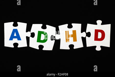 Quattro pezzi di un puzzle con lettere ADHD su sfondo nero. L' ADHD è disturbo da deficit di attenzione e iperattività. Foto Stock