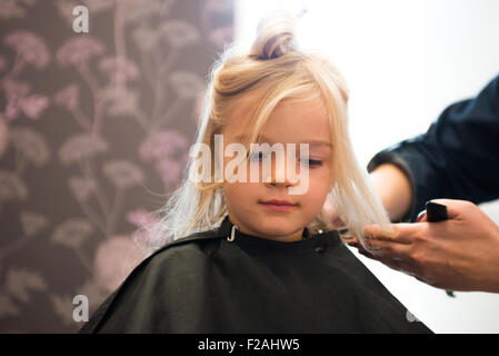 Parrucchiere femmina il taglio e la spazzolatura bambino giovane ragazza bionda capelli nel salone di parrucchiere Foto Stock