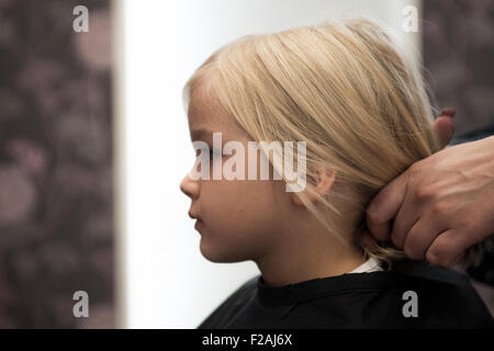 Parrucchiere femmina il taglio e la spazzolatura bambino giovane ragazza bionda capelli nel salone di parrucchiere Foto Stock