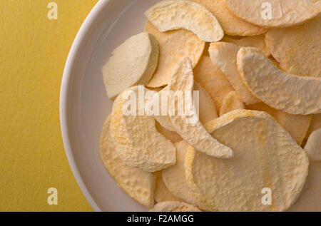 Top vista ravvicinata di pesche secche le fette su un piatto in cima a un giallo tavolo illuminato con luce della finestra. Foto Stock