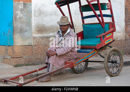 Vecchio pousse malgascio-pousse driver, in attesa per i clienti nelle vie della città Antsirabe, Vakinankaratra, Madagascar, Africa Foto Stock