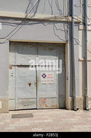 Grigio acciaio verniciato porte di garage che sfocia in una strada asfaltata. Vi è un parcheggio non firmare sulle porte. Scutari, Shkodër, Albania Foto Stock